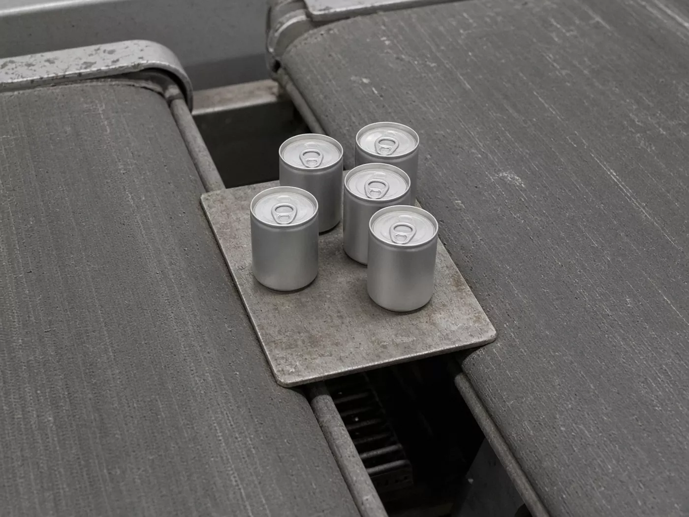 Plain cans on a metal plate that spans a gap between two conveyor belts